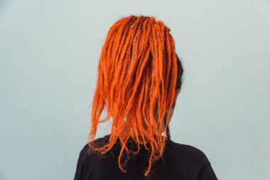 Kırmızı saçlı kız beyaz arka planda kuyruk şeklinde toplandı. Kafasında uzun kazayağı olan genç bir kadın. Turuncu rastalı ve piercingli gayri resmi kızlar.
