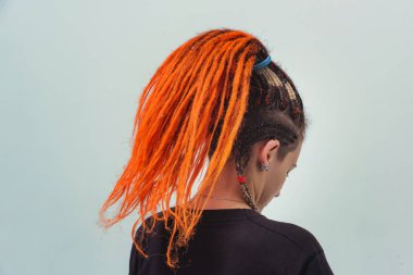 Kırmızı saçlı kız beyaz arka planda kuyruk şeklinde toplandı. Kafasında uzun kazayağı olan genç bir kadın. Turuncu rastalı ve piercingli gayri resmi kızlar.