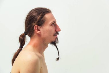 Uzun saçlı ve sakallı beyaz arka planda çıplak gövdeli bir adam. Uzun saçlı, at kuyruklu ve sakallı bir adam..