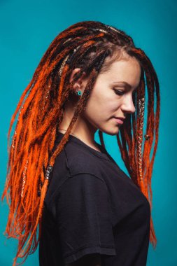 Deniz dalgası arkaplan renginde kırmızı ateş saçan kız. Mavi arka planda turuncu rastalı ve piercingli genç bir kadın. Güzel, cüretkar, gayri resmi, kırmızı sarı saçlı bir kızın resmi.