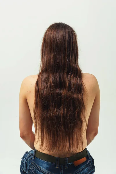 A man with long hair with naked torso on white background rear view from the back . Long flowing hair of a young boy. Care for long men\'s hair
