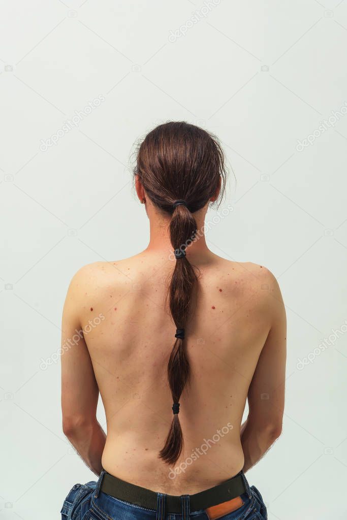 A man with long hair and a beard with a naked torso on white background rear view in profile. Long hair to the back collected in the tail. A man with long hair sits on a chair