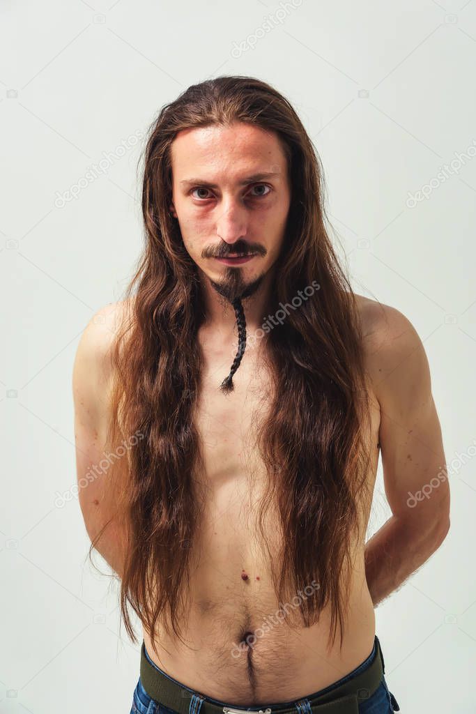 A man with long hair and a beard with a naked torso on a white background. Long flowing hair of a young boy. Care for long men's hair