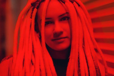 Kırmızı ışıkta siyah beyaz rastalı kız. Kırmızılı rastalı, gayri resmi görünümlü genç bir kadın. Kırmızı neonlu kıza uzun saplı.