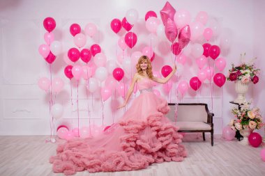 Balonların arka planında pembe balo elbisesi giyen genç bir kadın. Pembe ve beyaz balonlu Bulut elbisesi içinde güzel bir kız. Kızda havalı balo elbisesi var.