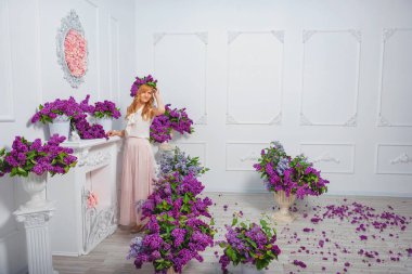 Leylakların arka planında başında çelenk olan uzun etekli bir kız. Mor çiçeklerin arka planında gülümseyen güzel bir kız. Kız ve bahar leylağı