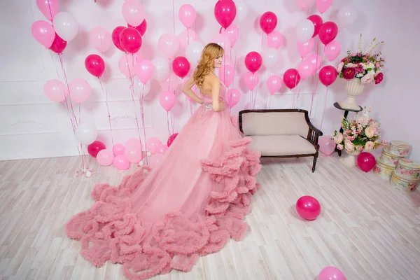 A young woman in a pink ball gown on a background of balloons. Beautiful girl in evening puffy Cloud dress with pink and white balloons. Air lush ball gown on the girl