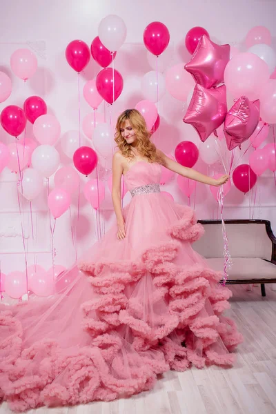 A young woman in a pink ball gown on a background of balloons. Beautiful girl in evening puffy Cloud dress with pink and white balloons. Air lush ball gown on the girl