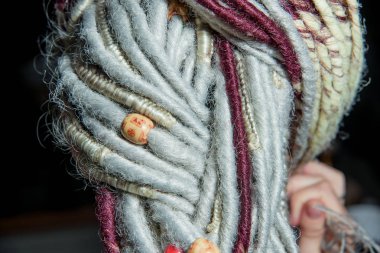 Boncuklar ve örgülerle desenleri süslemek. Renkli yapay saçlı kız. Beyaz ve Burgundy rastaları genç bir kadının başındaki gerçek saçlar. Gayri resmi kültürden bir kızın görüntüsü.