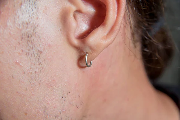 Earring close-up. A small earring pierced men\'s ear. The guy with the pierced ears