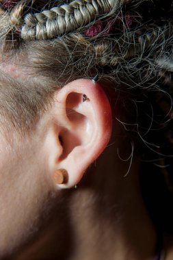 Rastalı bir kızın kulağını delmek. Küpeli bir kadın kulağı. Yakından. Gayri resmi kültürden bir kızın görüntüsü.