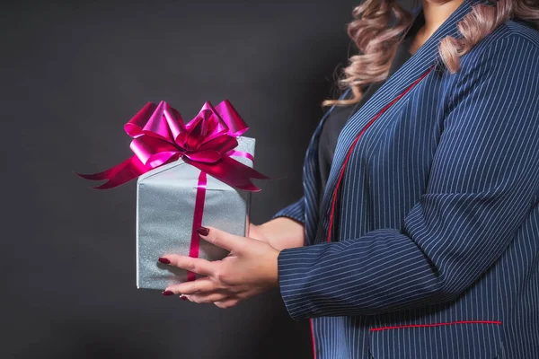 Gift box in female hands closeup. A box in silver wrapping paper with a purple bow and ribbon in the hands of a woman. Christmas gift in hands close up