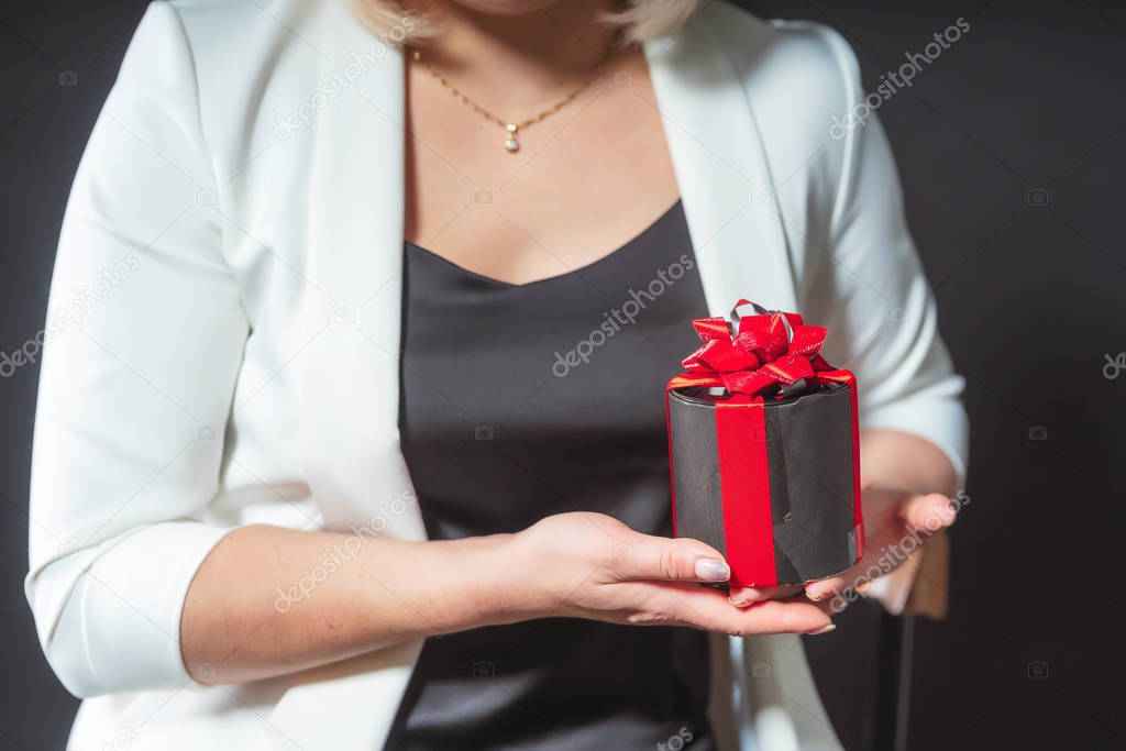 Gift box in female hands closeup. Black box with a red bow in the hands of the girl. Christmas gift in hands close up