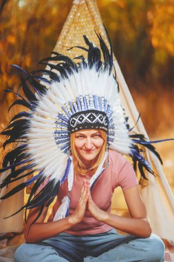 Kafasında Kızılderili hamamböceği olan bir kız. Hint kostümü giymiş genç bir kadın. Kotlu ve tişörtlü bir kızın Feather Heather adresi