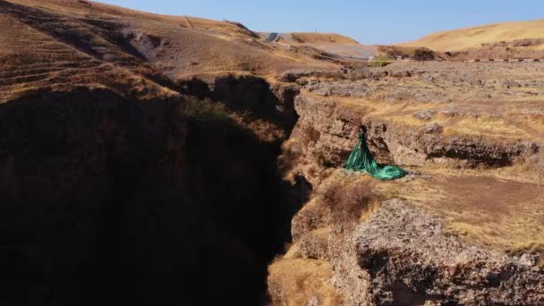 南カザフスタンの航空ビューのアクス峡谷の緑のドレスの女性 岩の背景におとぎ話の夜のボールのガウンの若い女性 山の中の長いドレスの美しい女の子 — ストック動画