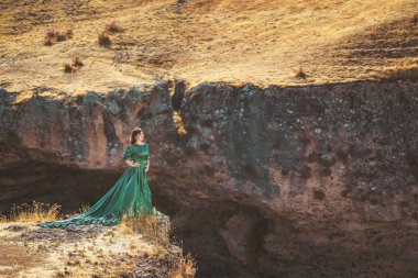 Güney Kazakistan 'daki Aksu Kanyonu' nda yemyeşil elbiseli bir kadın. Peri masalı gibi bir gece elbisesi giymiş genç bir kadın. Kayaların ve dağların arkasında. Dağlarda uzun elbiseli güzel bir kız.