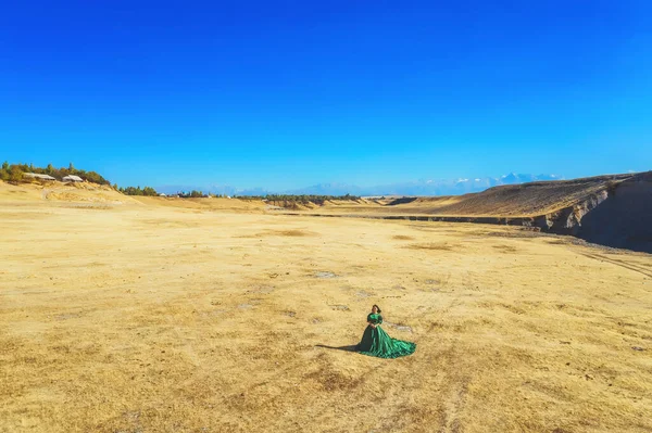 Woman in green dress on the background of mountains in south Kazakhstan. Young woman in  fairy tale ball gown on background of mountains and yellow steppe. Beautiful girl in long dress in mountains