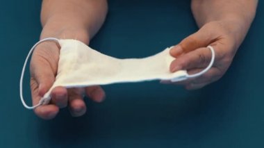 Yaşlı bir kadının ellerinde gazlı bez maskesi. Tıbbi maske takan yaşlı bir kadının elleri. Gazlı bezden yapılmış ev yapımı tıbbi maske.