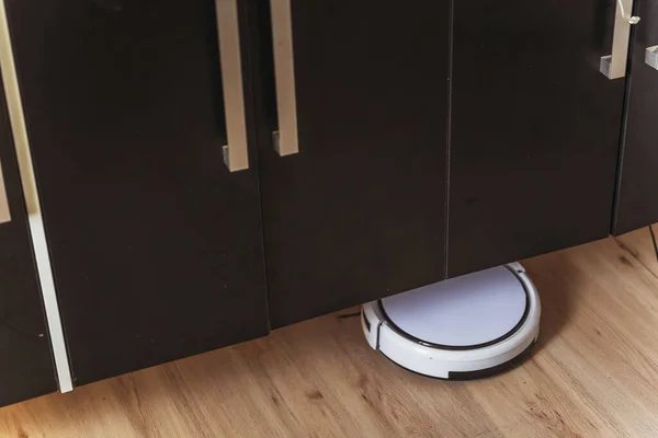 White robot vacuum cleaner at the base. Robot vacuum cleaner in the house on the floor under the closet. Modern small vacuum cleaner
