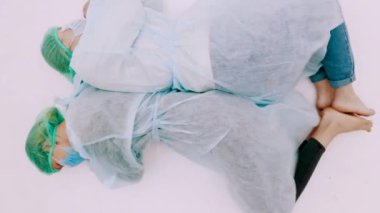 Koruyucu takım elbiseli ve yüz maskeli iki kadın. Genç kızlar koruyucu sağlık önlükleri, kepleri ve maskeleriyle beyaz zeminde yatıyorlar. Grip salgını trajedisi