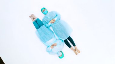 Koruyucu takım elbiseli ve yüz maskeli iki kadın. Genç kızlar koruyucu sağlık önlükleri, kepleri ve maskeleriyle beyaz zeminde yatıyorlar. Grip salgını trajedisi