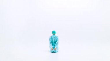 Koruyucu tıbbi giysiler ve yüz maskeleri takan bir kadın. Koruyucu sağlık önlükleri, kepleri ve maskeleriyle beyaz bir zeminde diz çökmüş bir adam. Grip salgını trajedisi