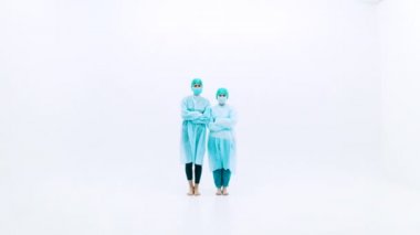 Koruyucu takım elbiseli ve yüz maskeli iki kadın. Genç kızlar koruyucu sağlık önlükleri, kepleri ve maskeleriyle beyaz arka planda yan yana dururlar. Grip salgını trajedisi