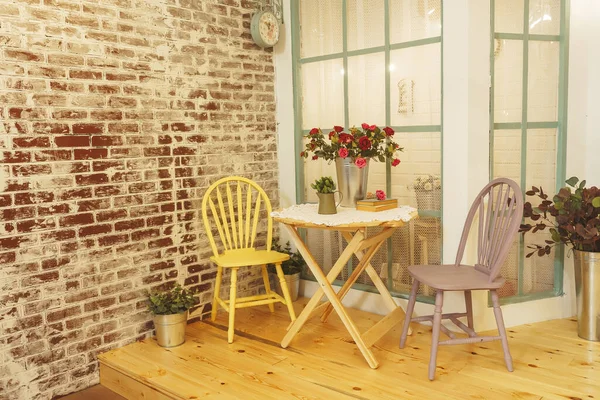 Summer porch with garlands of light bulbs. Terrace of the summer house design of the photo Studio. A verandah patio with flowers roses in metal buckets and wooden chairs and a table.