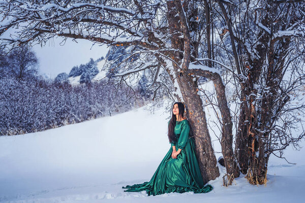 Девушка в сказочном длинном зеленом платье в заснеженных горах. Женщина в сказочном платье в горах зимой. Зимняя сказочная фотосессия красивой девушки в Сайрам су Казахстан
