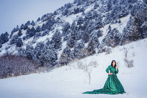 Девушка в сказочном длинном зеленом платье в заснеженных горах. Женщина в сказочном платье в горах зимой. Зимняя сказочная фотосессия красивой девушки в Сайрам су Казахстан
