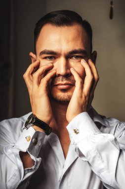 Beyaz gömlekli Asyalı bir adam ellerini yüzünün önünde tutuyor. Yüz ve ellerin yakın plan genç erkek portresi. Gömlekli ve elinde saati olan bir iş adamı.