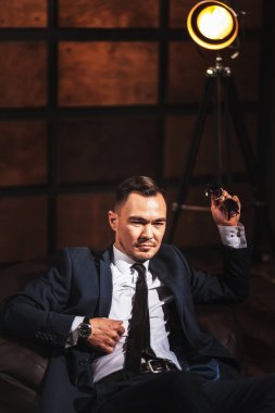 Beyaz gömlekli ve takım elbiseli bir adamın portresi. Ellerinde gözlük, koyu ahşap bir arka planda. Güzel, şık, seksi, flörtçü erkek tavan arası tarzı bir odada portre. Genç Asyalı beyefendi