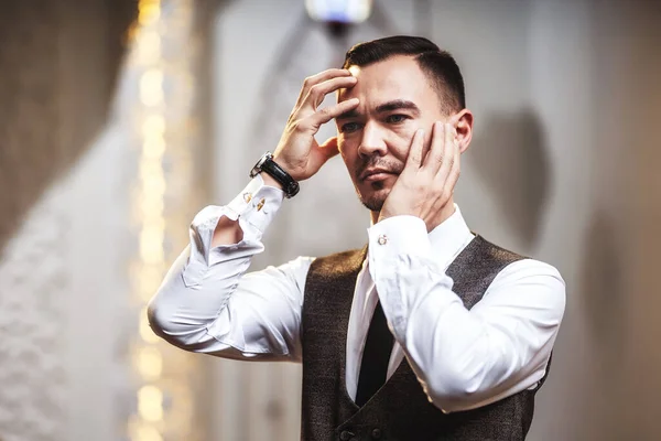 An Asian man in a white shirt holds his hands in front of his face. Young cute male model beautiful close-up portrait of face and hands. A businessman in a shirt and with a watch on his hand on a light white background