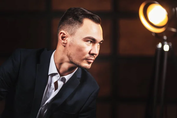 Portrait of a man in a white shirt and suit on a dark wooden background. Beautiful stylish men\'s business portrait in a loft-style room. Young handsome Asian businessman