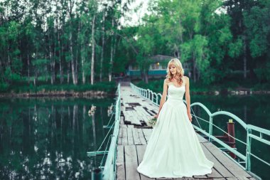 Gölün üzerindeki eski köprüde gelinlikli bir kız. Göldeki ormanda beyaz elbiseli bir kadın. Yeşil ağaçların arka planına karşı uzun elbiseli gelin