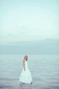 Beyaz gelinlikli bir kız suyun içinde duruyor. Kırgızistan 'da Issyk Kul Gölü kıyısında beyaz elbiseli bir kadın. Gelin göl kıyısında