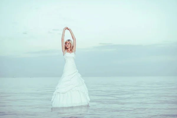 A girl stands in the water in a white wedding dress. A woman in a white dress on the shore of lake Issyk Kul in Kyrgyzstan. Bride near the lake river