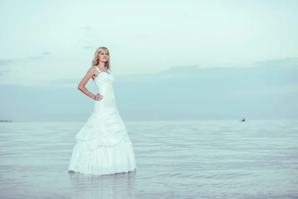 A girl stands in the water in a white wedding dress. A woman in a white dress on the shore of lake Issyk Kul in Kyrgyzstan. Bride near the lake river