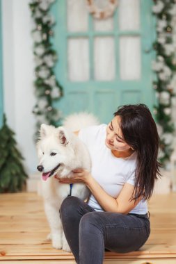 Noel süslemelerinin arka planında köpekli bir kız var. Noel verandasında beyaz köpeği olan bir kadın. Beyaz köpekli Asyalı kadın.