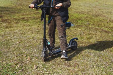 Parktaki çimlerin üzerinde oturan bir kız Scooter 'a biniyor. Motosikletli bir çocuk. Baharın başında motosikletli bir çocuk.