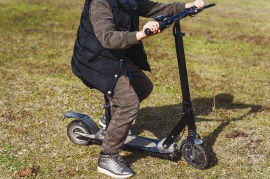 Parktaki çimlerin üzerinde oturan bir kız Scooter 'a biniyor. Motosikletli bir çocuk. Baharın başında motosikletli bir çocuk.