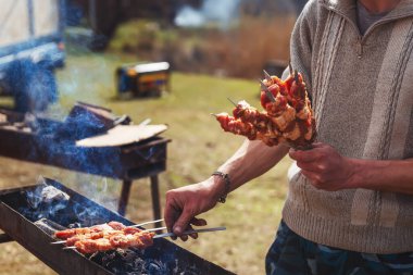 Bir adam dışarıdaki doğada barbekü kızartır. Bir insanın elindeki şişte çiğ kebap eti. Shashlik ile aile pikniği
