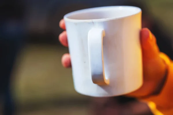 White ceramic mug in hand. A Cup of tea in a woman\'s hand. A mug in a woman\'s hand.