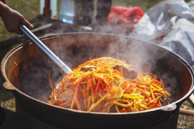 Dışarıda piknikte büyük bir kazanda pilav pişirmek. Özbek bayram pilavı pişiriyorum. Havuç ve et bir kazanda pilav için büyük bir kazanda canlı ateşte pirinçle birlikte.