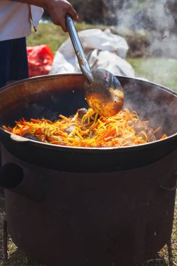 Dışarıda piknikte büyük bir kazanda pilav pişirmek. Özbek bayram pilavı pişiriyorum. Havuç ve et bir kazanda pilav için büyük bir kazanda canlı ateşte pirinçle birlikte.