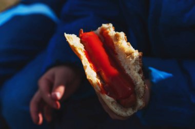 Tatilde ev yapımı sosisli sandviç. Ekmek arası sosis, ketçaplı tortilla. Ekmek ve sosis bir adamın ellerinde.