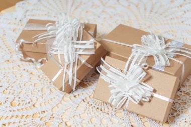 Kare sandık hediye kutuları ve masanın üzerinde kar kaplı koniler. Beyaz kurdeleli açık kahverengi karton kutular ve Noel hediyeleri. Yeni yıl hediyeleri beyaz örgü bir masa örtüsünde