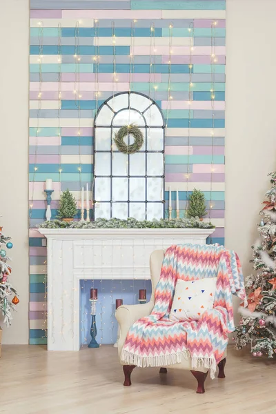 A room with a Christmas decoration in pink blue and white tones. A chair near the fireplace and the Christmas tree. Two Christmas trees in the living room luxury design.