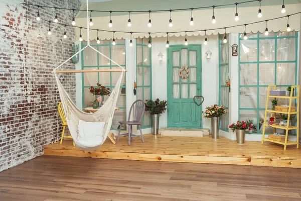 Evin verandasının arka planında Wicker salıncak hamağı var. Ampullü salıncak ve yaz terası retro çelenkler. Bir fotoğraf stüdyosunda bahar süslemeleri olan güzel bir veranda.