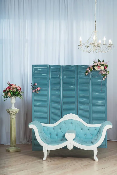 Light blue classic sofa on the background of a folding screen in the living room. White living room in a classic style with a blue piano. Spring summer interior decoration